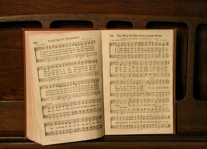 Aufgeschlagenes altes Gesangbuch mit vergilbten Notenseiten auf dunklem Holztisch.