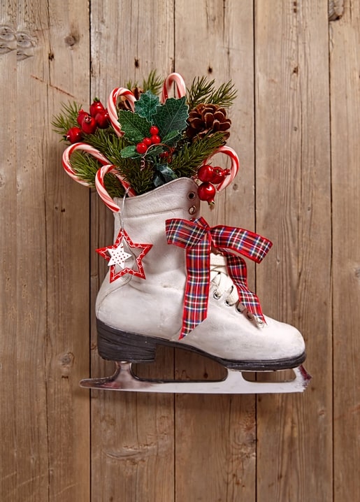 White vintage ice skate filled with pine branches, holly, berries, and candy canes