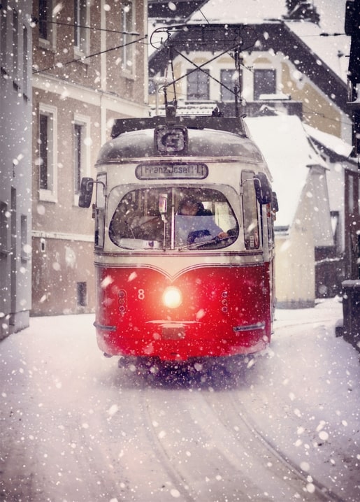 Vintage red tram with glowing headlight driving through heavy snowfall on a European street
