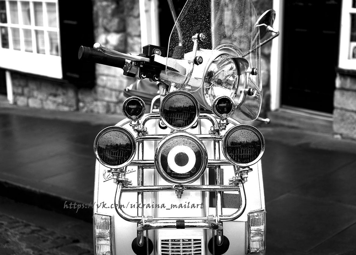 Schwarz-weißes Nahaufnahme-Foto der verchromten Front eines Vintage-Rollers mit Zusatzscheinwerfern