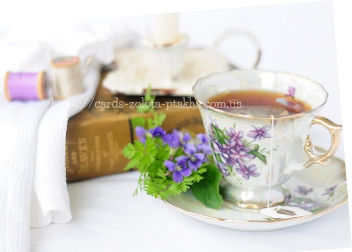 Vintage-Blumen-Teetasse mit Tee neben Veilchen, alten Büchern und Garnrollen