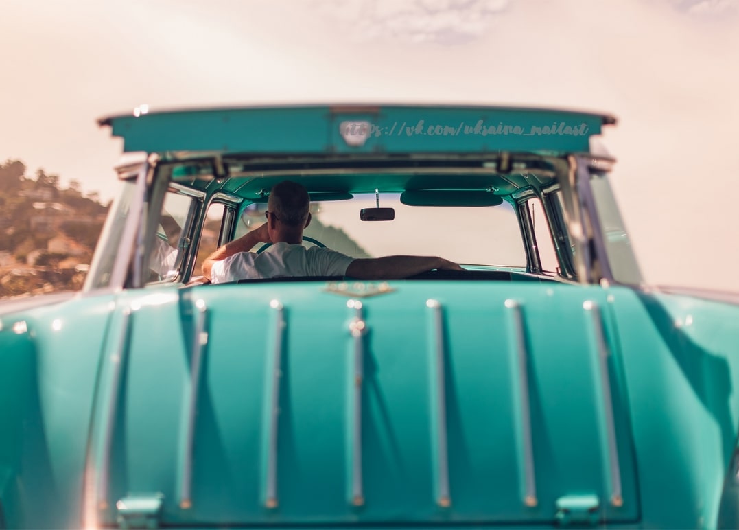 Rückansicht eines türkisfarbenen Oldtimers, Fahrer unterwegs zur Küste bei Sonnenuntergang