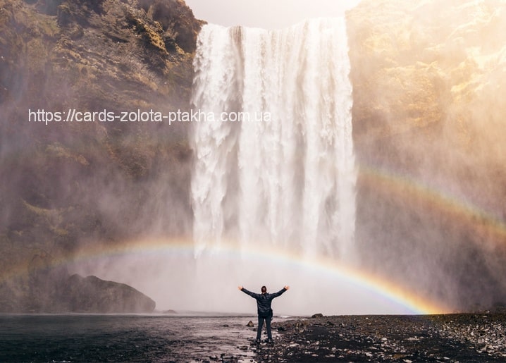 Wasserfall mit vollem Regenbogen und einem Wanderer mit erhobenen Armen