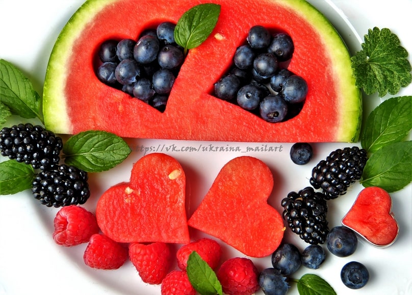 Wassermelonenscheiben und Heidelbeeren in Herzform, umgeben von Brombeeren und Himbeeren