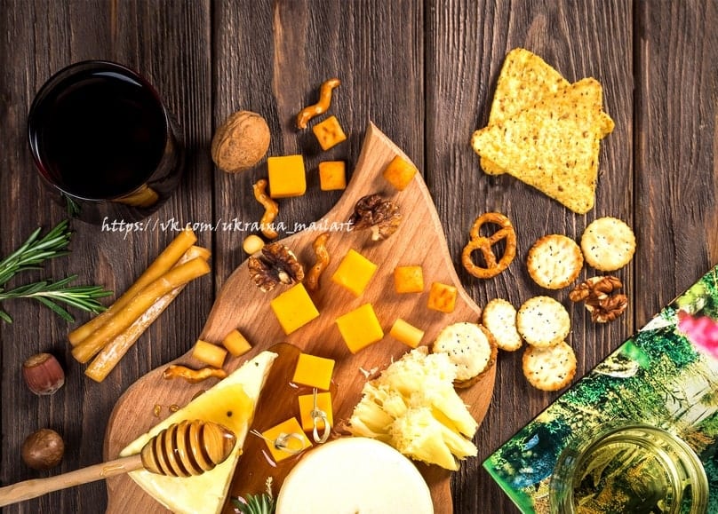 Overhead view of cheese cubes, pretzels, crackers, walnuts, and honey drizzle with a glass of red wine