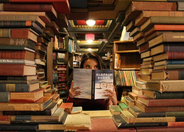 Дівчина читає книжку серед високих стосів старих книг, що утворюють тунель