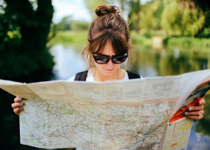 Junge Frau mit Sonnenbrille liest eine Landkarte am See