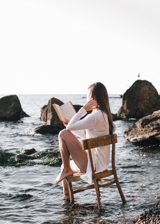 Жінка читає книгу, сидячи на стільці в мілкій морській воді