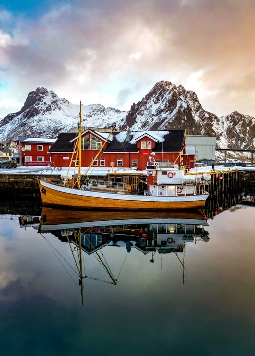 Hölzernes Fischerboot spiegelt sich vor schneebedeckten Bergen im Wasser