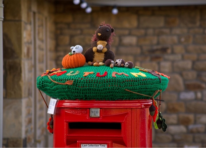 Roter britischer Postbox mit gehäkelter grüner Herbstmütze, Kürbis, Igel und Eicheln
