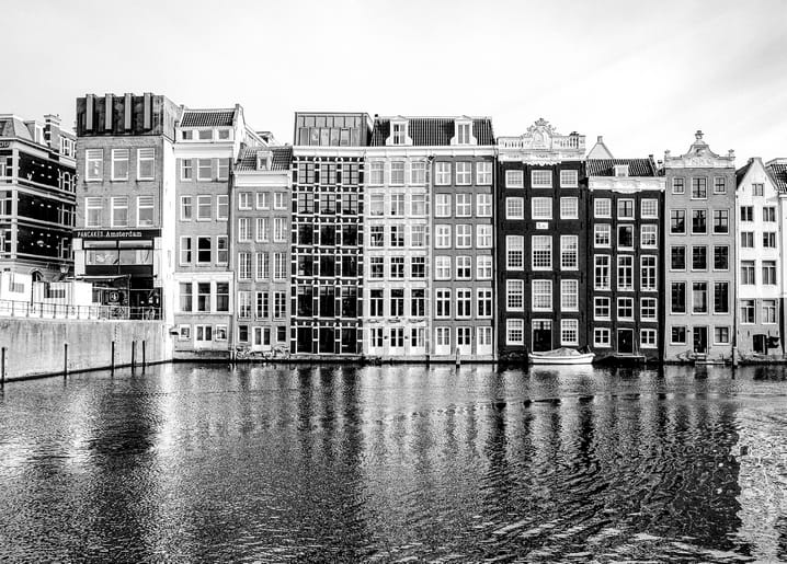 Schwarz-weißer Blick auf Amsterdamer Grachtenhäuser mit Giebeln und Spiegelung im Wasser