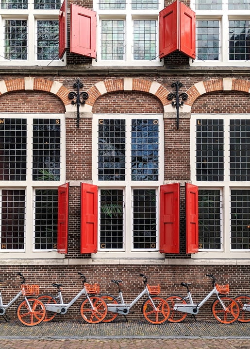 Backsteinfassade in Amsterdam mit roten Fensterläden und einer Reihe Fahrräder