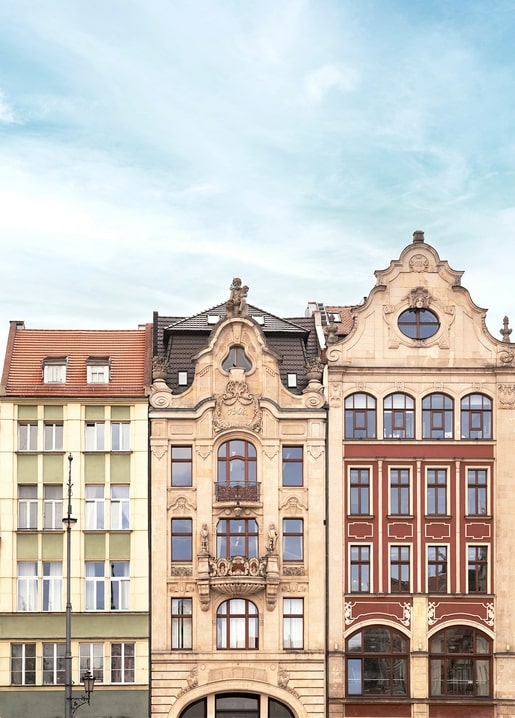 Ornate gabled townhouse facades in pastel tones under a summer sky