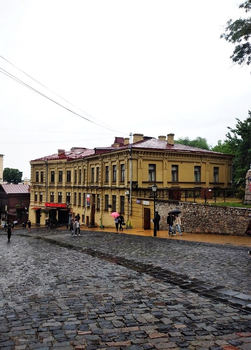 Regnerische Straße am Andriivsky Uzviz mit gelbem Haus und Regenschirmen in Kiew