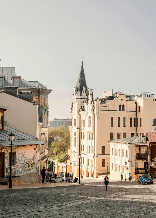 Kopfsteinpflasterstraße in Kiew mit turmartigem Schlossgebäude und pastellfarbenen Häusern