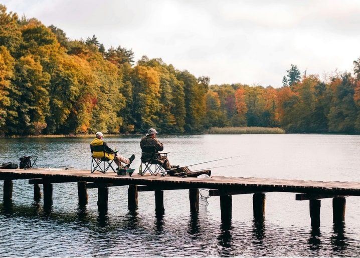 Zwei Männer angeln von einem Holzsteg auf einem See, umgeben von buntem Herbstwald