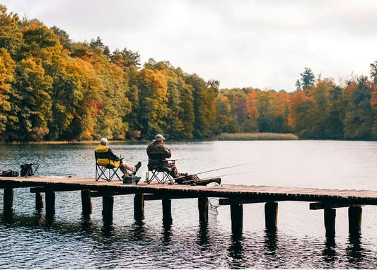 Zwei Männer angeln von einem Holzsteg auf einem See, umgeben von buntem Herbstwald