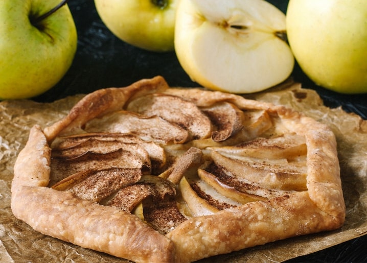 Rustikale Apfelgalette mit Zimt neben frischen grünen Äpfeln