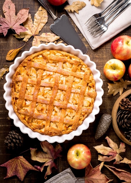 Lattice apple pie with fresh apples and maple leaves on a wood table