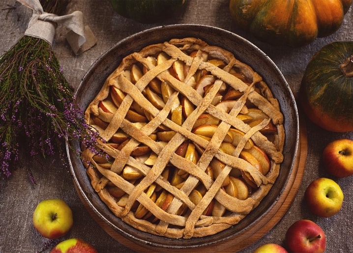Lattice-top apple pie surrounded by apples, pumpkins and dried lavender