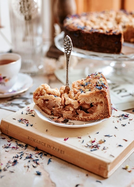 Slice of apple crumble pie with an antique fork on a floral plate atop a book