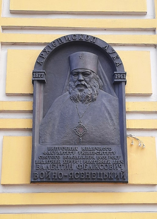 Bronze memorial plaque with portrait relief of Archbishop Luka on a yellow wall in Kyiv