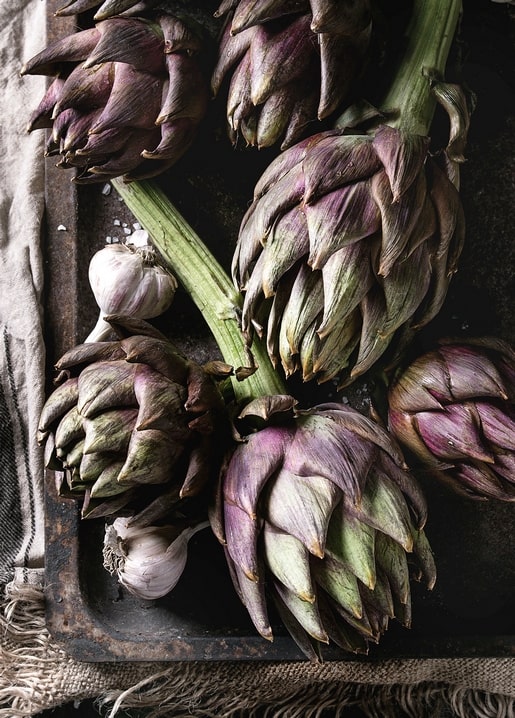 Violette Artischocken und Knoblauchzehen auf dunklem Backblech