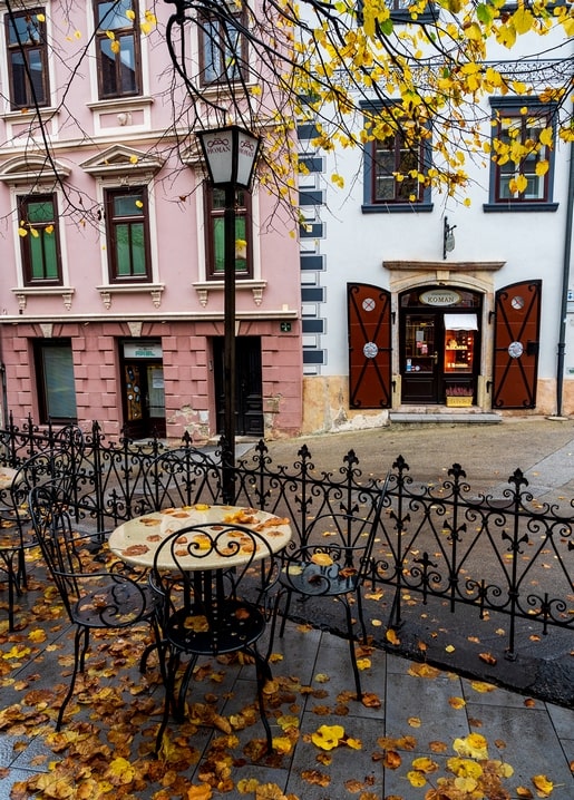 Wrought-iron café chairs and table on a cobbled street with pink buildings and a lamppost