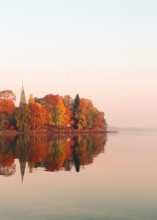Herbstlicher See mit hölzernem Kirchturm, gespiegelt im stillen Wasser bei Dämmerung