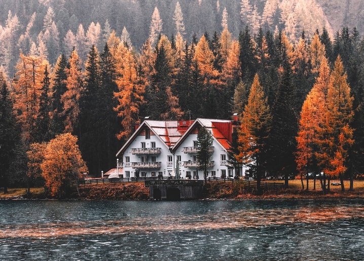 Weißes Chalet mit rotem Dach am nebligen See, umgeben von goldenen Lärchen