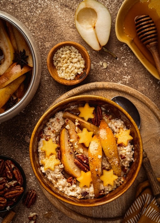 Schale Haferbrei mit karamellisierter Birne, Pekannüssen, Honig und Zimtsternen auf einem Holzbrett