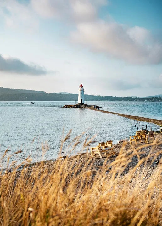 Autumn coastal photo postcard featuring a white lighthouse, calm sea, golden grasses and distant hills