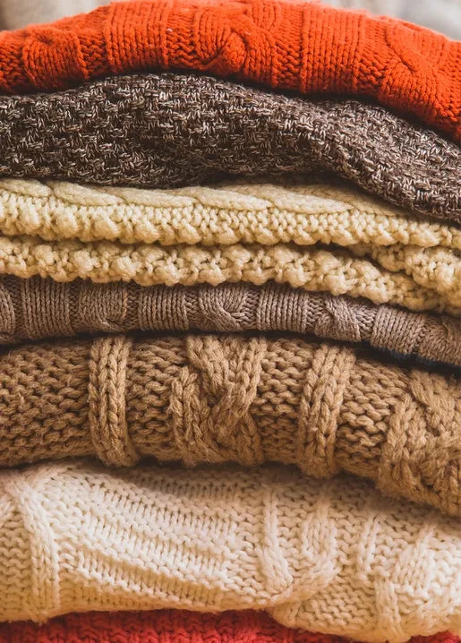 Cozy autumn photo postcard featuring a stack of knitted sweaters in warm neutral colors