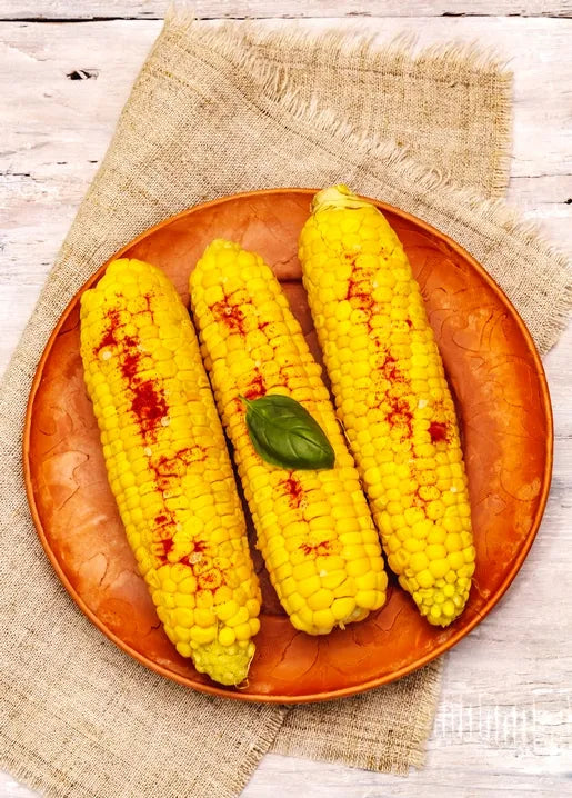Food postcard featuring three ears of corn on the cob with paprika and fresh basil