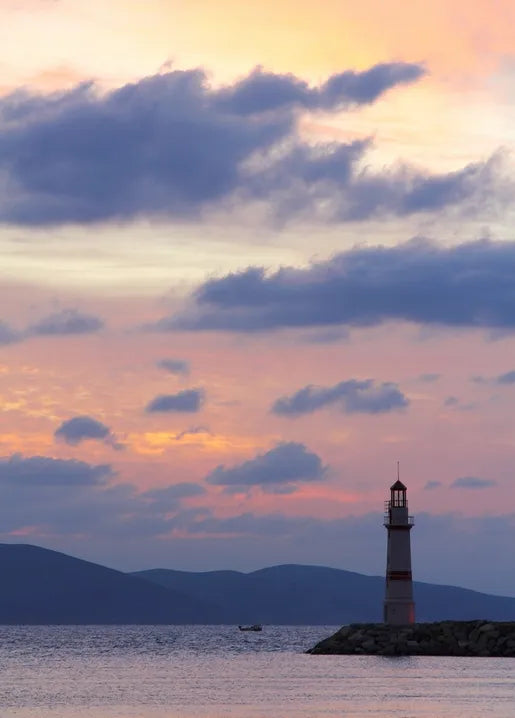 Coastal photo postcard featuring a lighthouse at sunset with calm sea and distant mountains