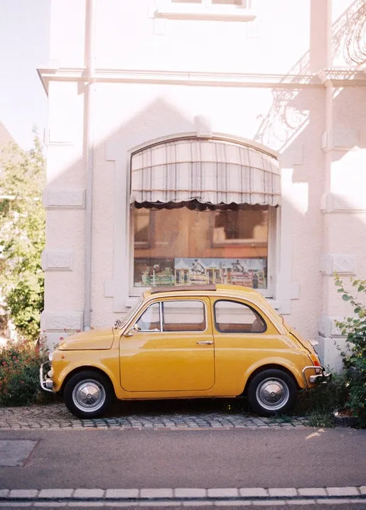 Vintage car photo postcard featuring a yellow Fiat 500 parked beside a European street