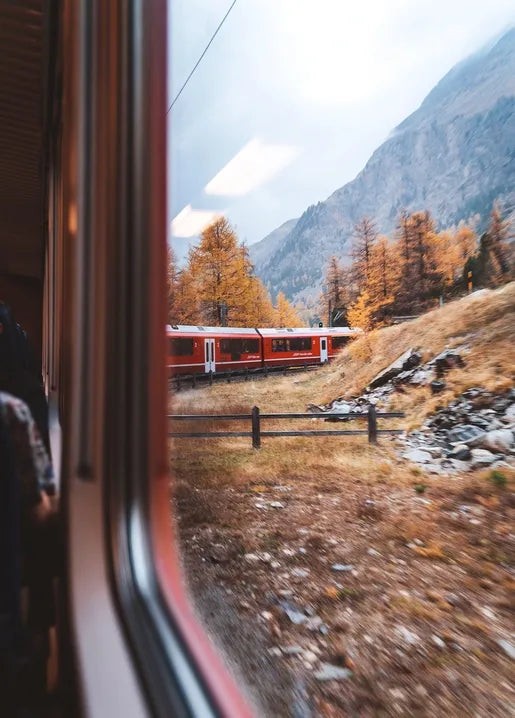Autumn travel photo postcard showing a red passenger train winding through golden mountains with early snow