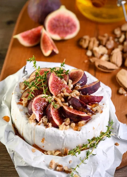 Food postcard featuring warm Brie topped with fresh figs, walnuts and thyme on a wooden board