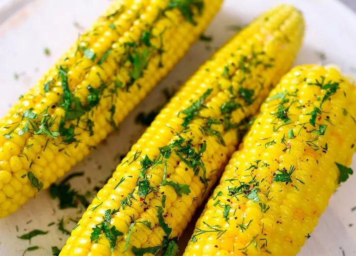 Food postcard featuring golden corn on the cob with melted butter and fresh green herbs