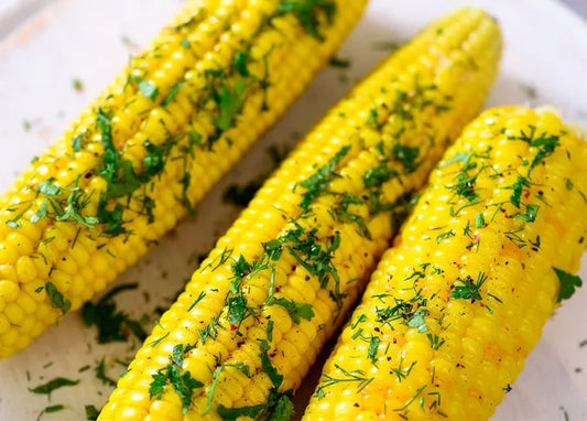 Food postcard featuring golden corn on the cob with melted butter and fresh green herbs