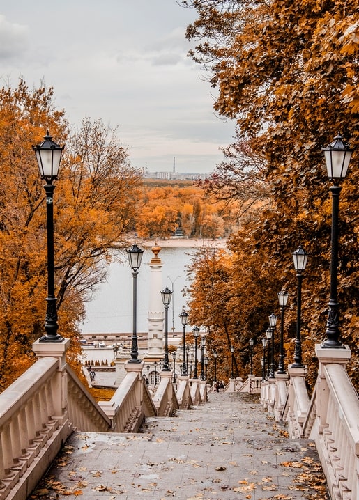 Steinerne Treppe mit Laternen führt durch Herbstlaub zum Fluss