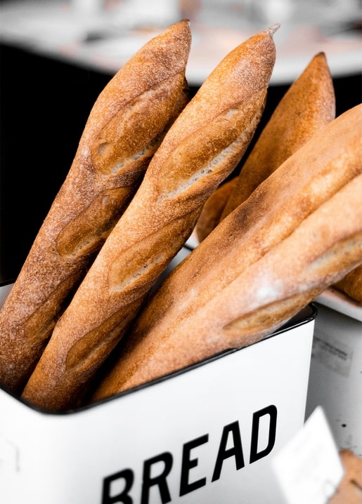 Crusty baguettes standing upright in a white bread bin