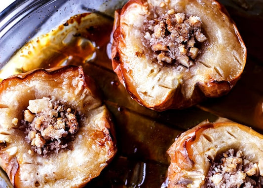 Baked apples stuffed with toasted nuts and brown sugar, glistening in caramel syrup