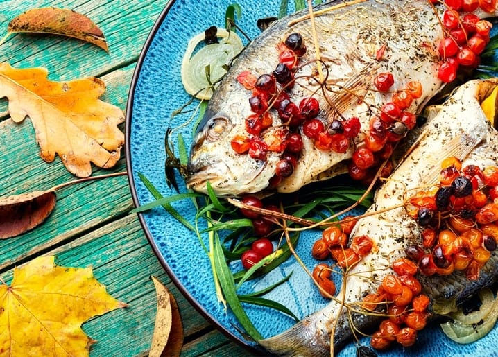 Gebratener Fisch mit Vogelbeeren auf blauem Teller, umgeben von Eichen- und Ahornblättern