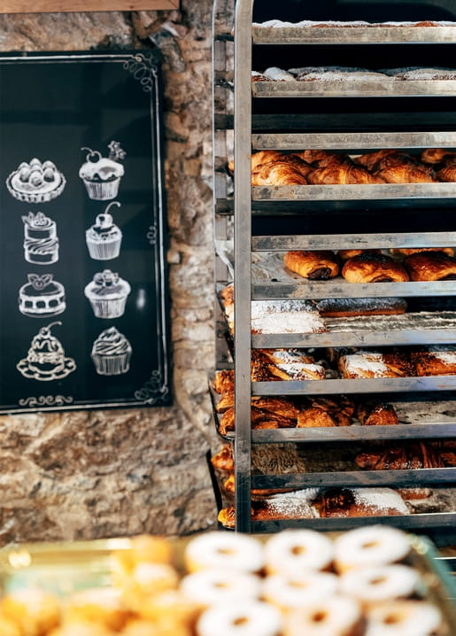 Goldene Croissants und Gebäck auf einem Bäckereiregal vor einer Steinwand mit Kreidetafel
