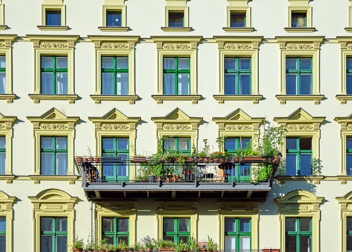 Altstadtfassade mit grünen Fensterrahmen und einem Balkon voller Topfpflanzen und Blüten