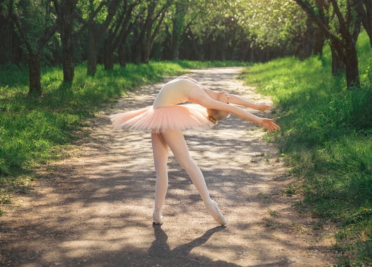 Ballerina in a pink tutu bending backward on a path beneath blossoming trees