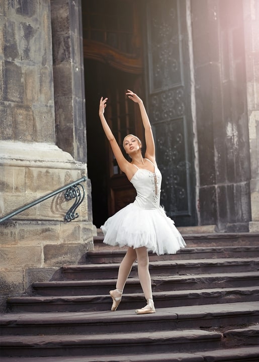 Ballerina in a white tutu dancing en pointe on stone steps of an ornate doorway