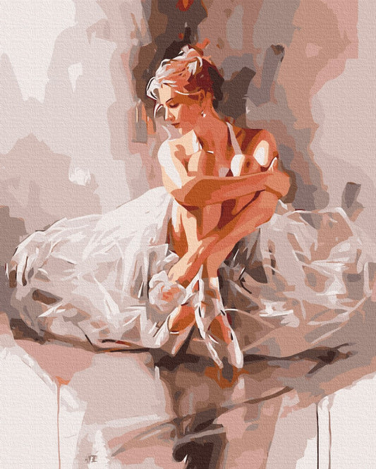 Seated ballerina in a white tutu tying the ribbon of her pointe shoe