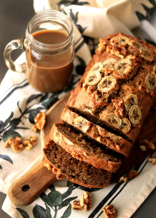 Aufgeschnittenes Bananenbrot mit Walnüssen und Karamellsauce auf einem Holzbrett mit Blumenserviette
